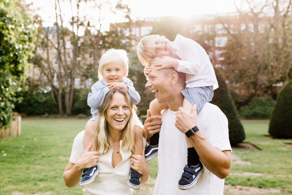 Outdoor family photo in Bristol with the children sitting on their parents shoulders and smiling   
