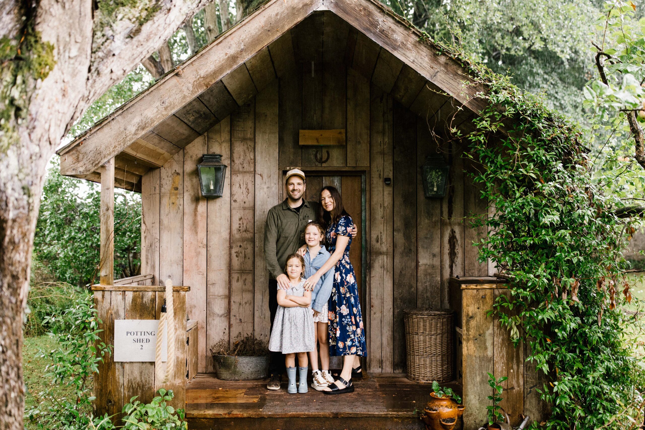 Outdoor family photo in Bristol standing in front of a wooden cabin surrounded by greenery 